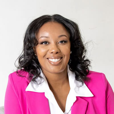 Dr. Jazlynn Paige headshot, a smiling black woman with long black hair in a half updo bun, wearing a grey blouse